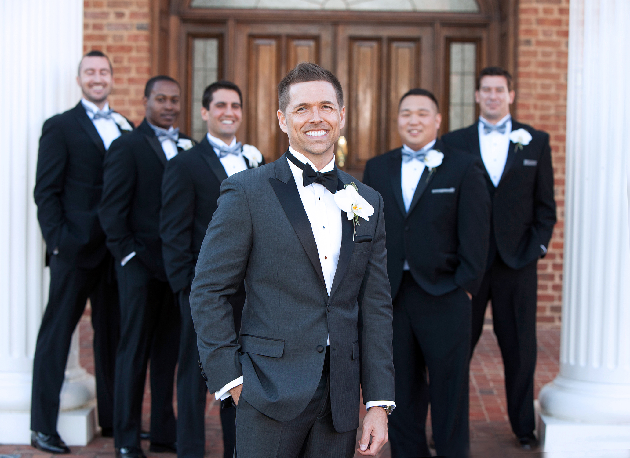 Men in elegant tuxedos pose for formal photograph