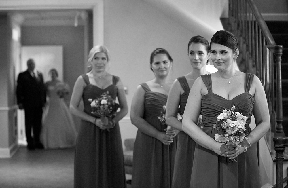 A bride and her bridesmaids, elegantly dressed, stand in a hallway, radiating joy and anticipation.