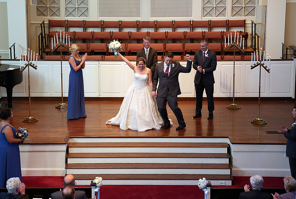 Newlyweds on stage, holding hands and smiling.
