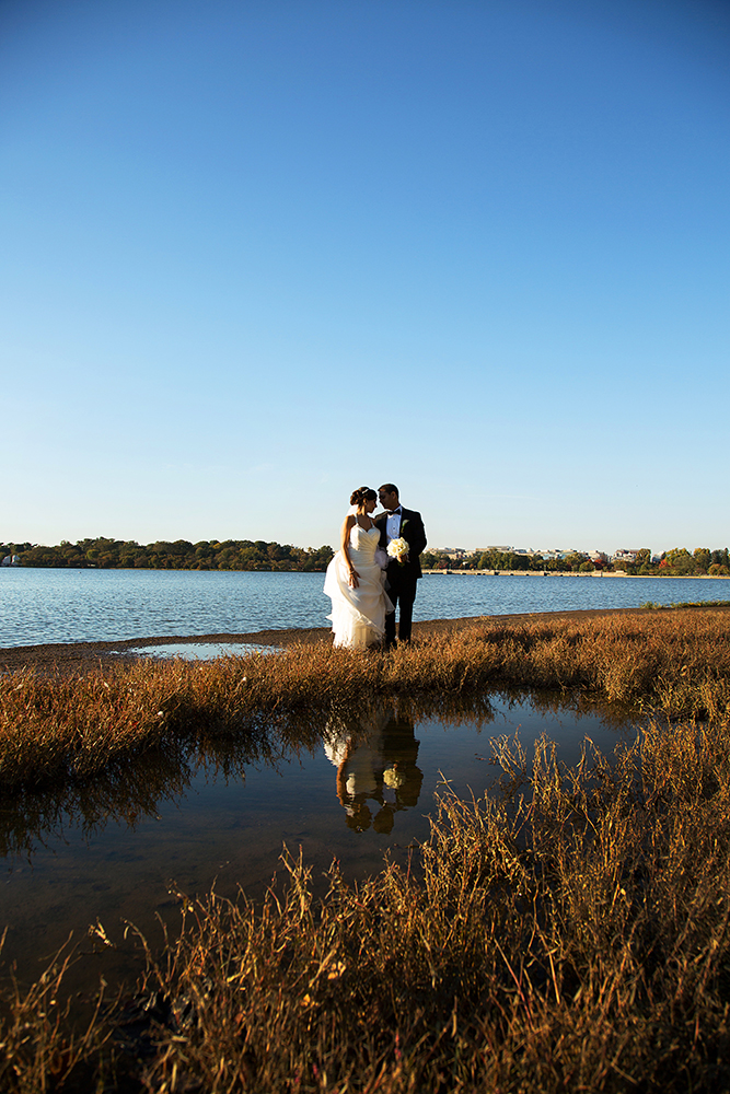 Newlyweds standing in shallow water near the shore on their wedding day.