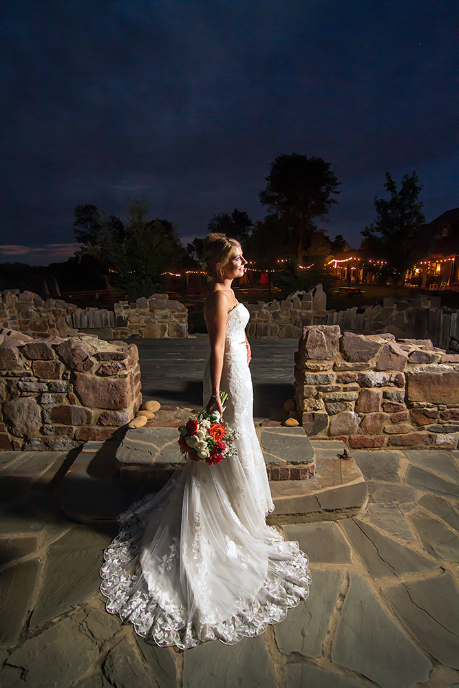 A bride gracefully stands on stone steps at night, exuding elegance and romance in the dimly lit ambiance.
