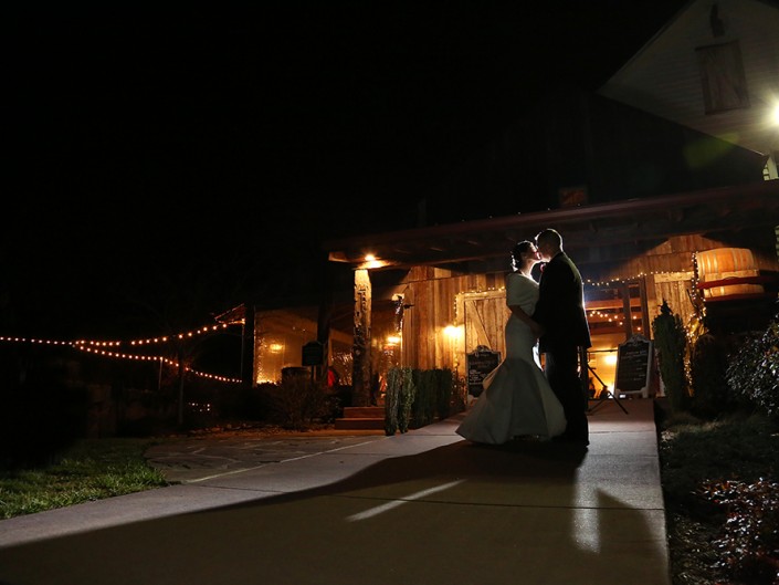 A newlywed couple stands together, smiling, as they pose for a nighttime photograph on their wedding day.