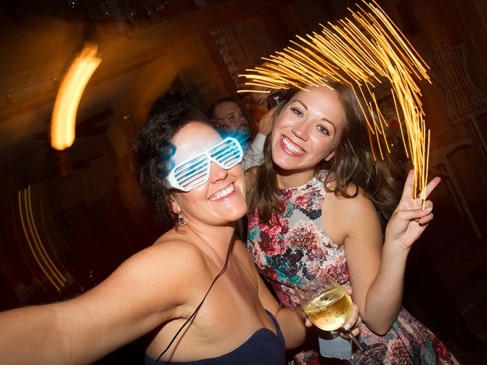 Two women wearing glasses, sharing smiles as they pose for a photo at a party.