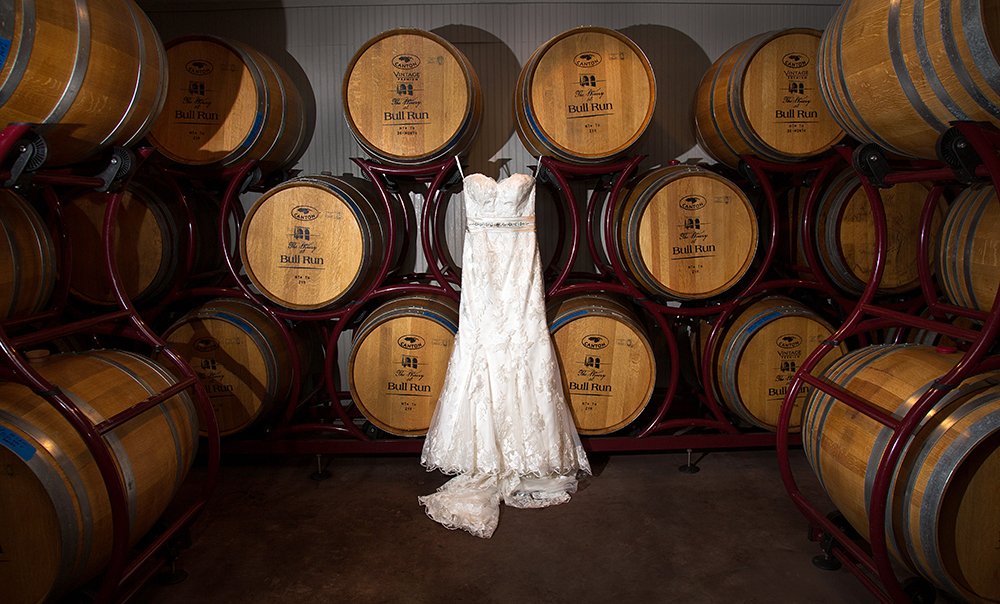Bridal gown on display amidst wine barrels.