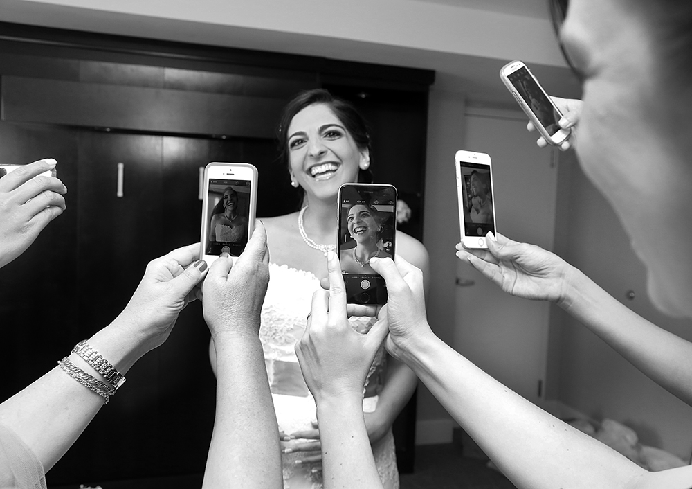 A bride capturing memories on her cellphone, radiating joy and elegance on her special day.
