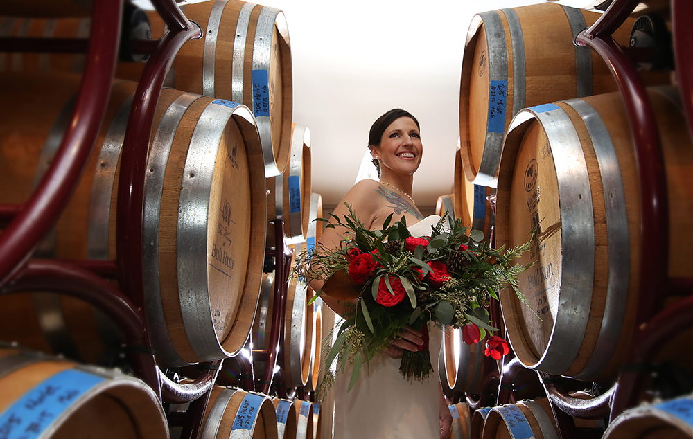 Bride with bouquet by wine barrels.