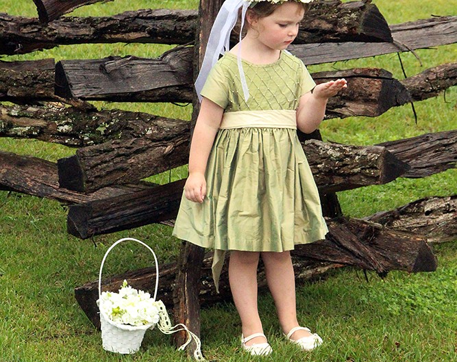 A young girl in a dress standing next to a fence, enjoying the outdoors.