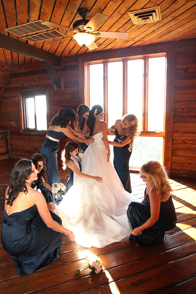 Women gather around a bride, helping her put on her wedding gown.