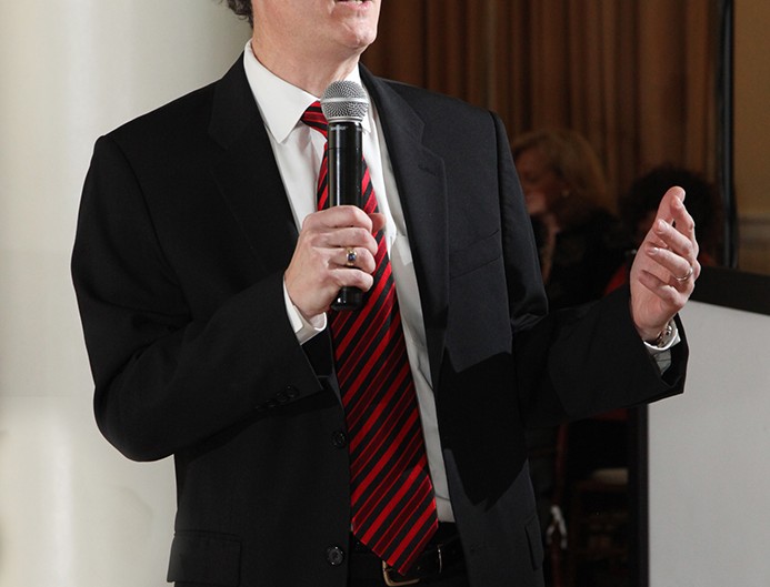 A confident professional man in a suit and tie, holding a microphone, ready to address an audience.