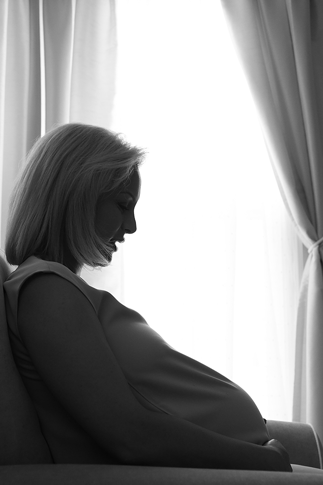 A pregnant woman sitting on a couch in front of a window
