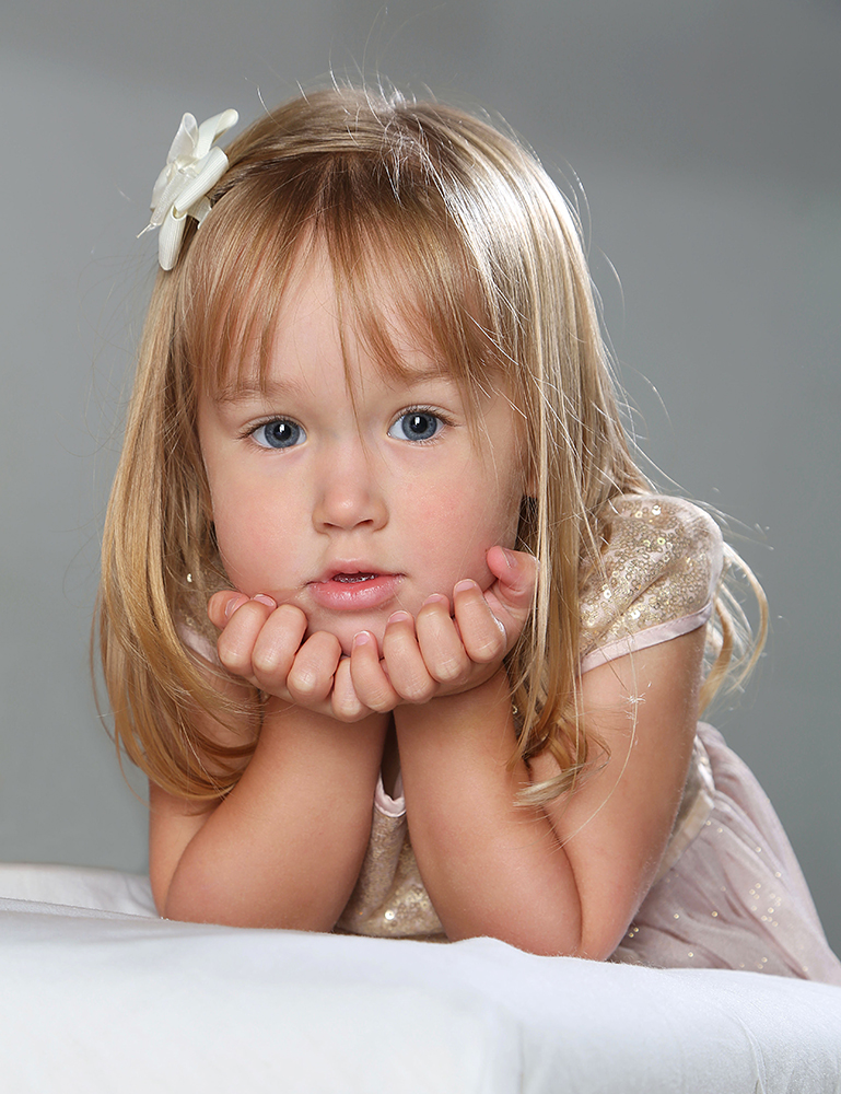 A young girl lying on a bed, deep in thought, with her hands gently resting on her chin.