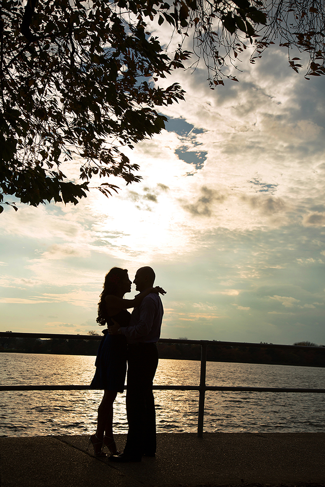 Two people kissing in front of a serene lake.