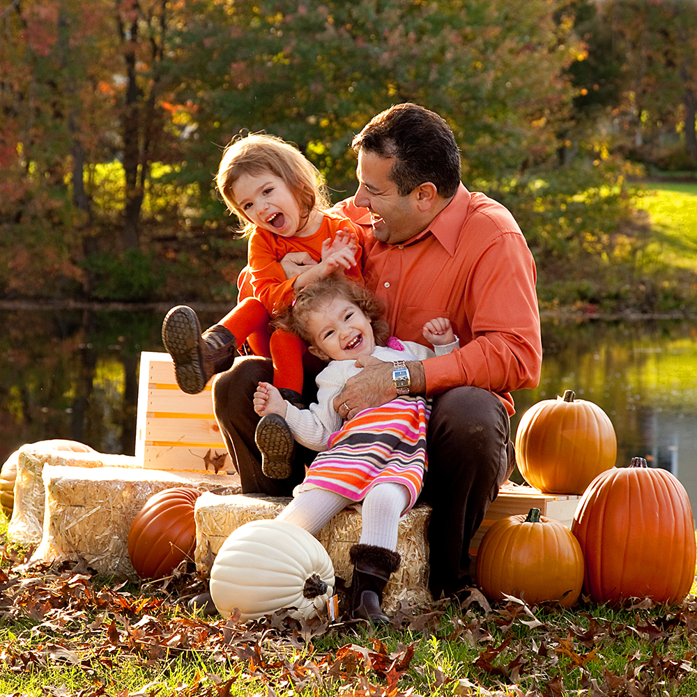 Father and daughters embrace autumn on pumpkin pile, capturing seasonal spirit