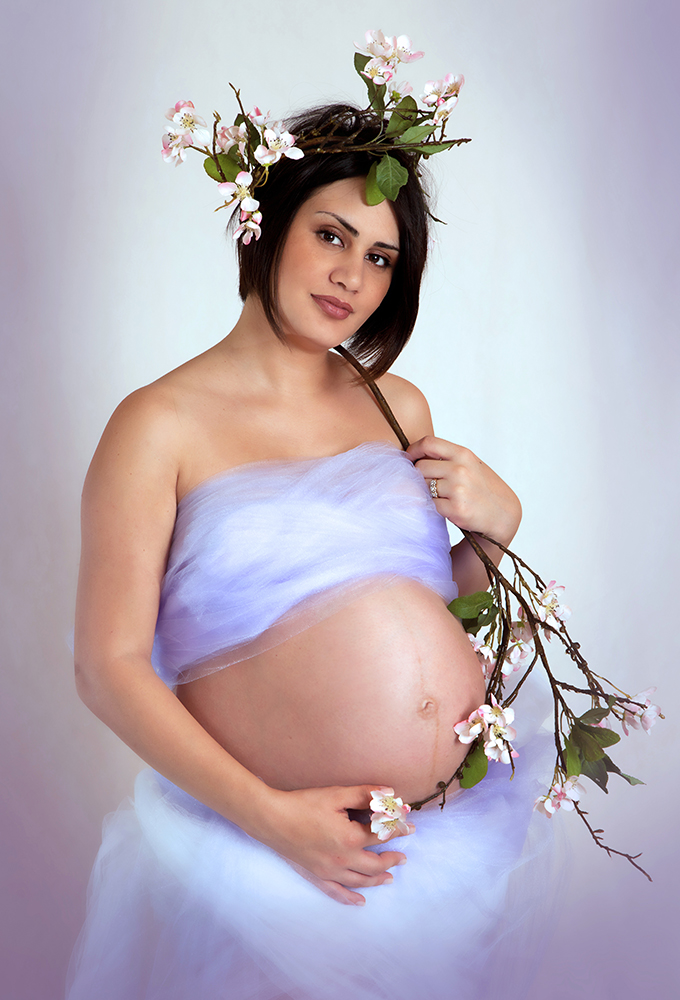 Pregnant lady in elegant dress gently cradling a beautiful flower