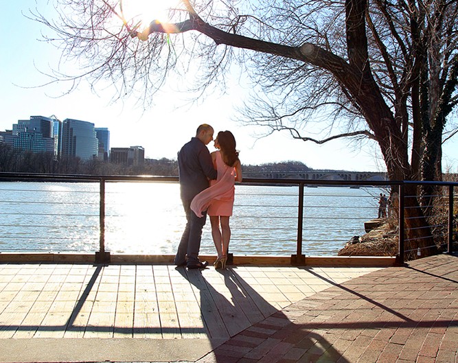 A loving couple sharing a kiss on a bench with a scenic water view.