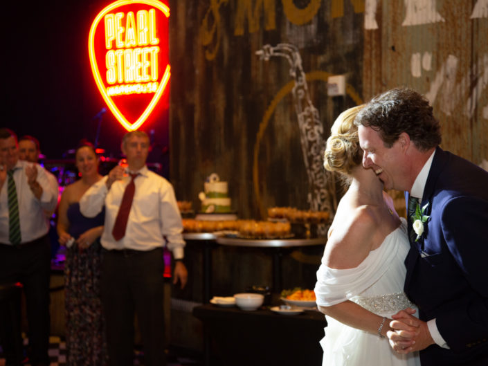 Newlyweds kissing in front of a vibrant neon sign.