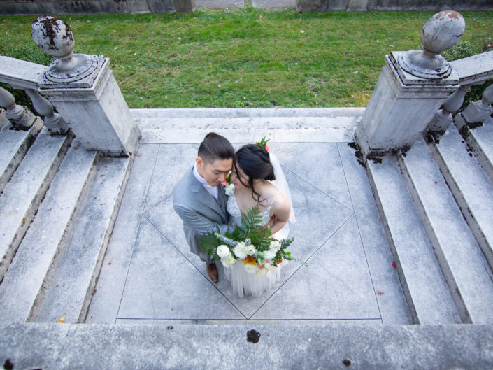 A newlywed couple stands on stone steps outside a building, radiating joy and love on their special day.