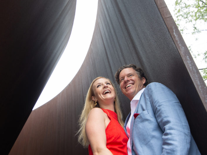 Couple smiling before a massive sculpture, captured in a photo.