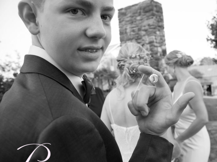 A young boy dressed in a formal tuxedo, holding a ring with a poised elegance and youthful charm.