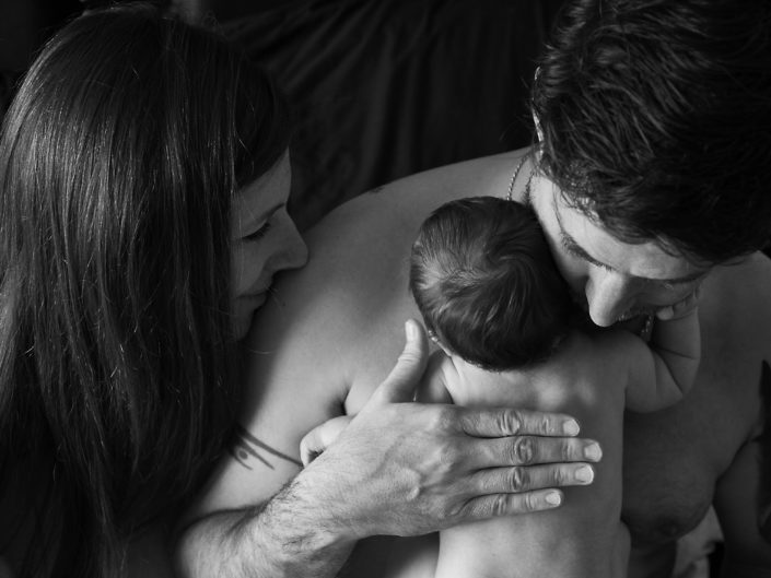 Couple embraces newborn in warm, cozy room, radiating love and warmth