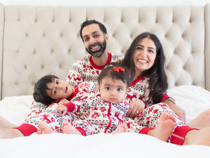 A family of four, donning matching pajamas, cozily rests on a bed.