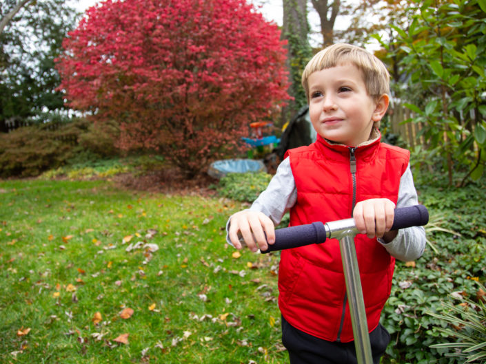 Boy joyfully riding a scooter in a grassy yard.