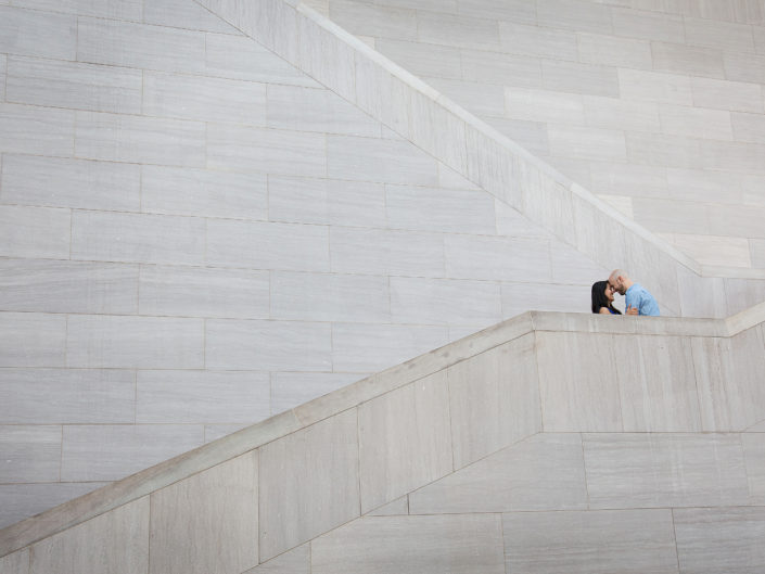 A couple stands on building stairs, exuding elegance and togetherness.