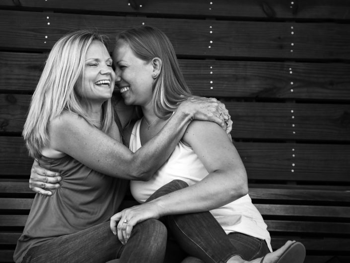Women embrace tightly on wooden bench, displaying friendship bond.