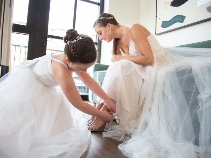 Bride helping bridesmaid with wedding shoes, a moment of friendship.