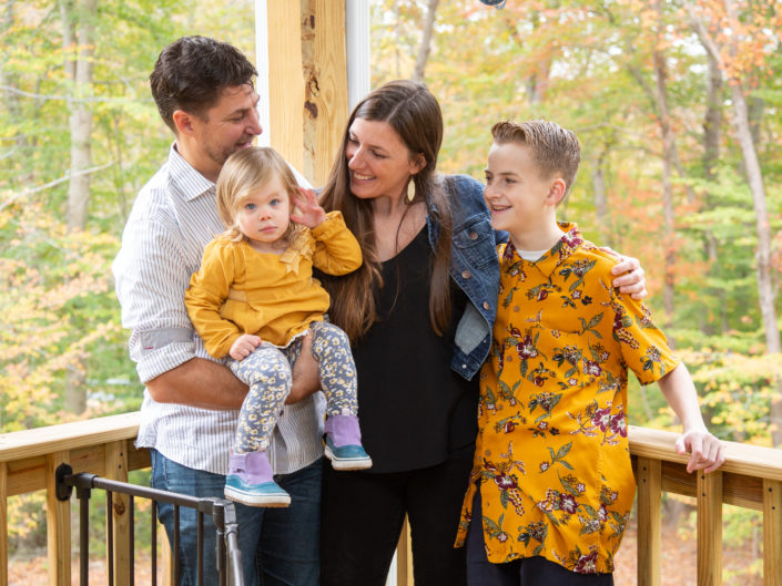 Family smiling on a porch, surrounded by autumn colors.