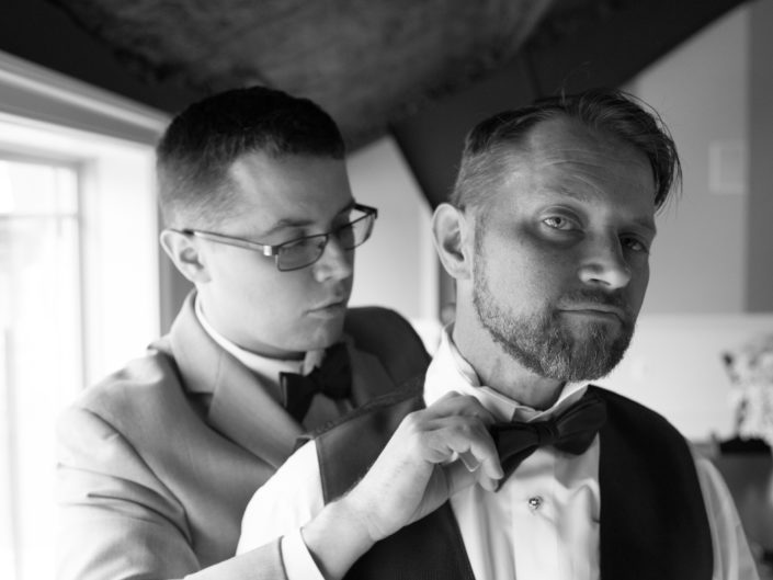 Men in elegant formal attire, adjusting bow tie and suit.
