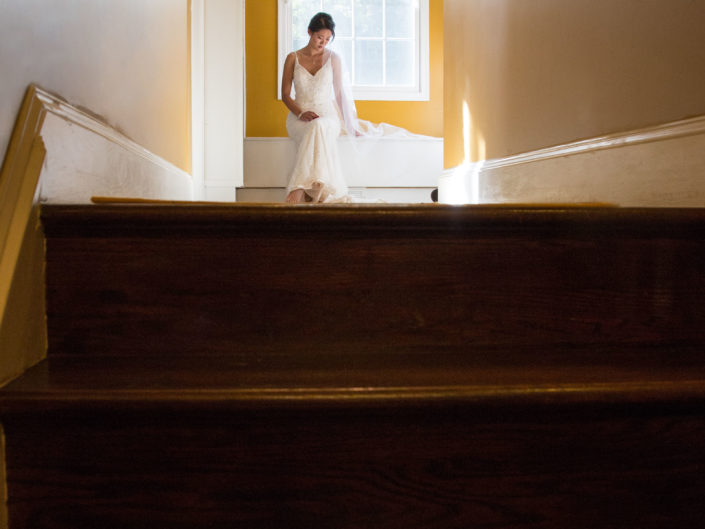 Bride in white gown posing on house stairs.