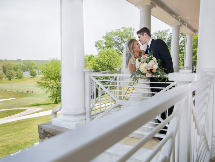 A bride and groom standing on a porch railing.