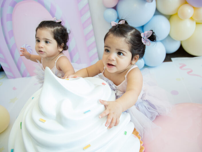 Two little girls playing with a cake in front of balloons.