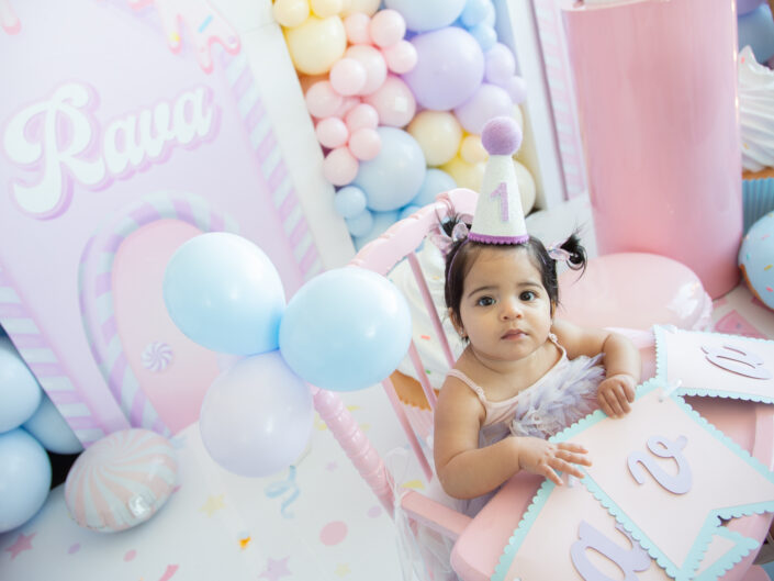 A little girl sitting in a chair in front of balloons.