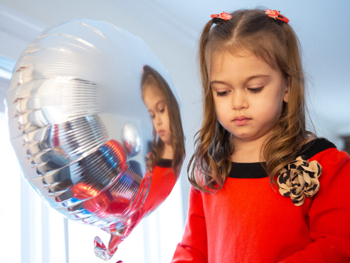 A little girl looking at a silver balloon.