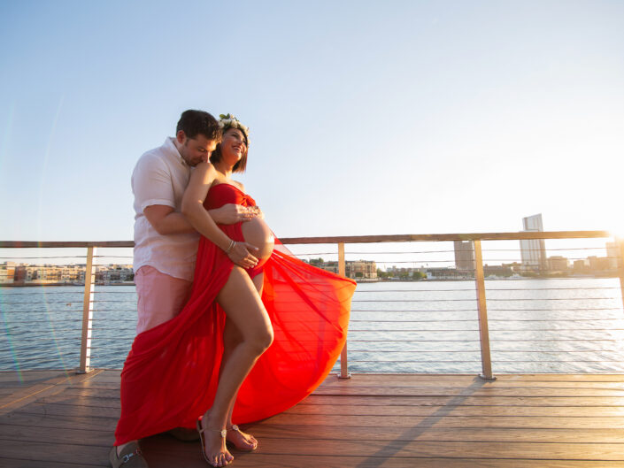 A couple in a red dress posing on a dock.