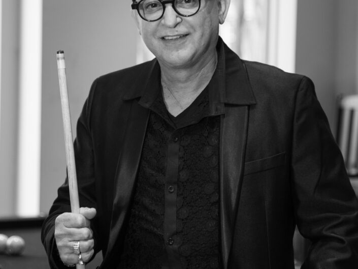 A black and white photo of a man with glasses and a pool cue.