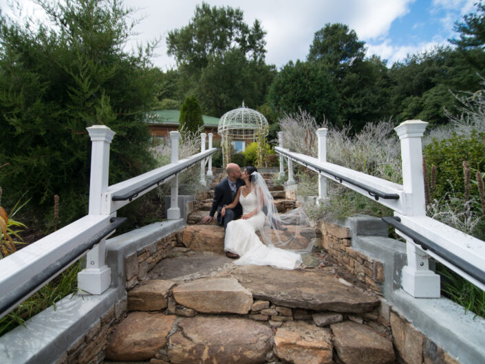A bride and groom kissing pose on the steps of a garden.