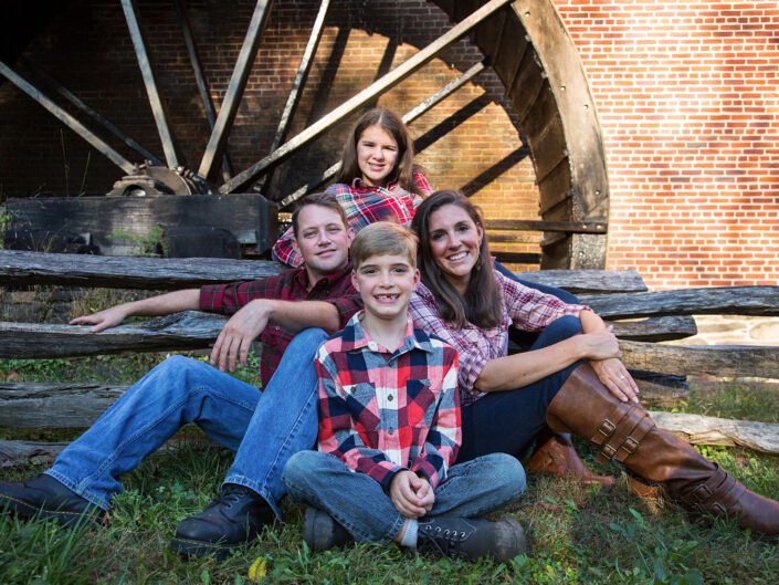 Smiling family seated in front of a wooden backdrop. Colvin Run Mill, Virginia