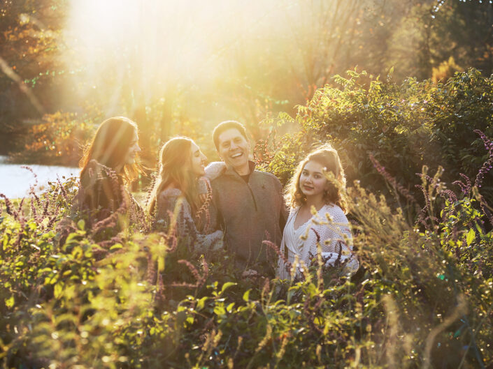Couple and daughters in greenery with sunlight in the background