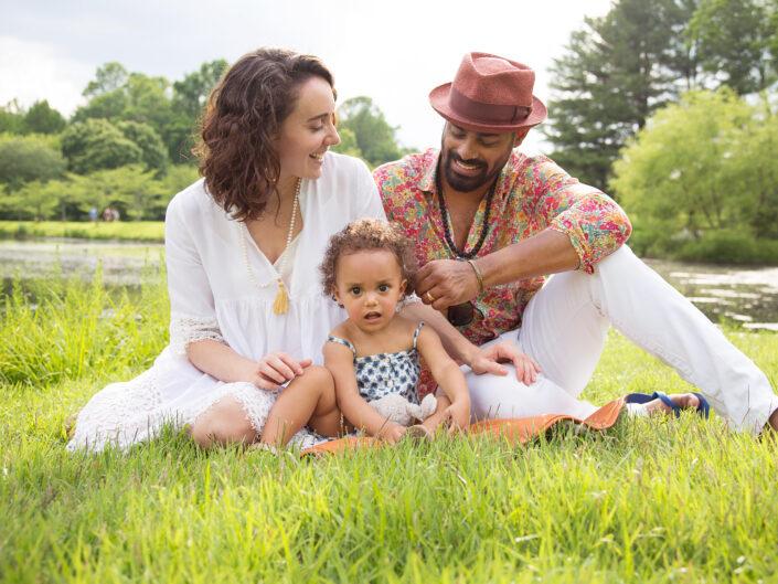 Family with a child laughing together while sitting on the grass.