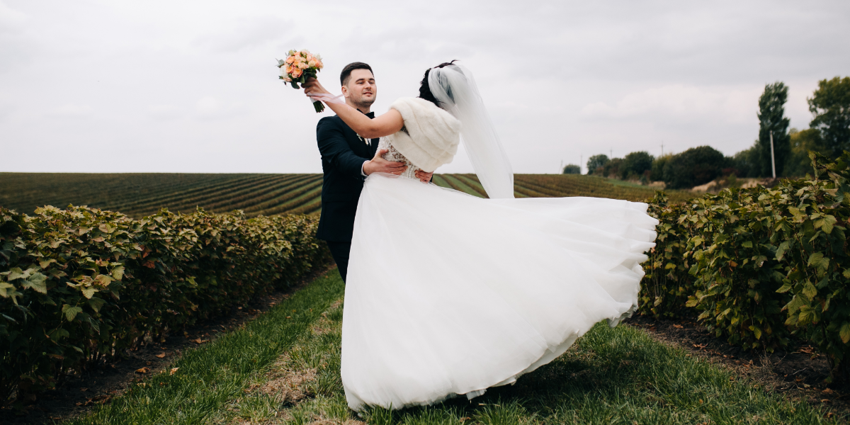 Couple in wedding attire sharing an romantic pose in a field.