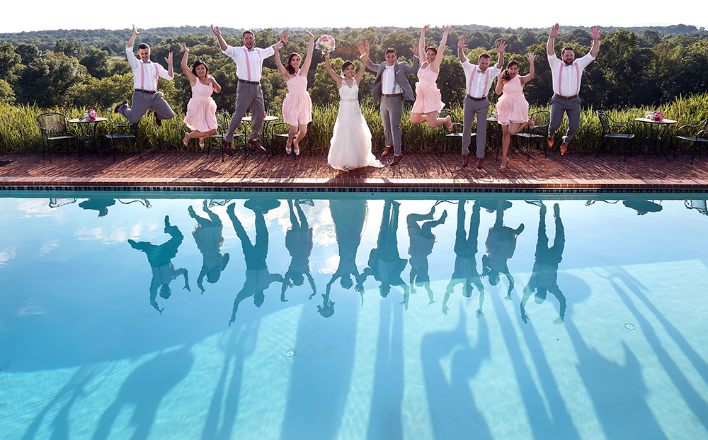 A group of guests jumping for a photo at a poolside wedding celebration.